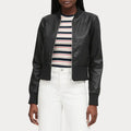 Person wearing a black leather jacket over a striped shirt with white pants on a light gray background