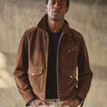 Man wearing a brown suede jacket against a textured wall.