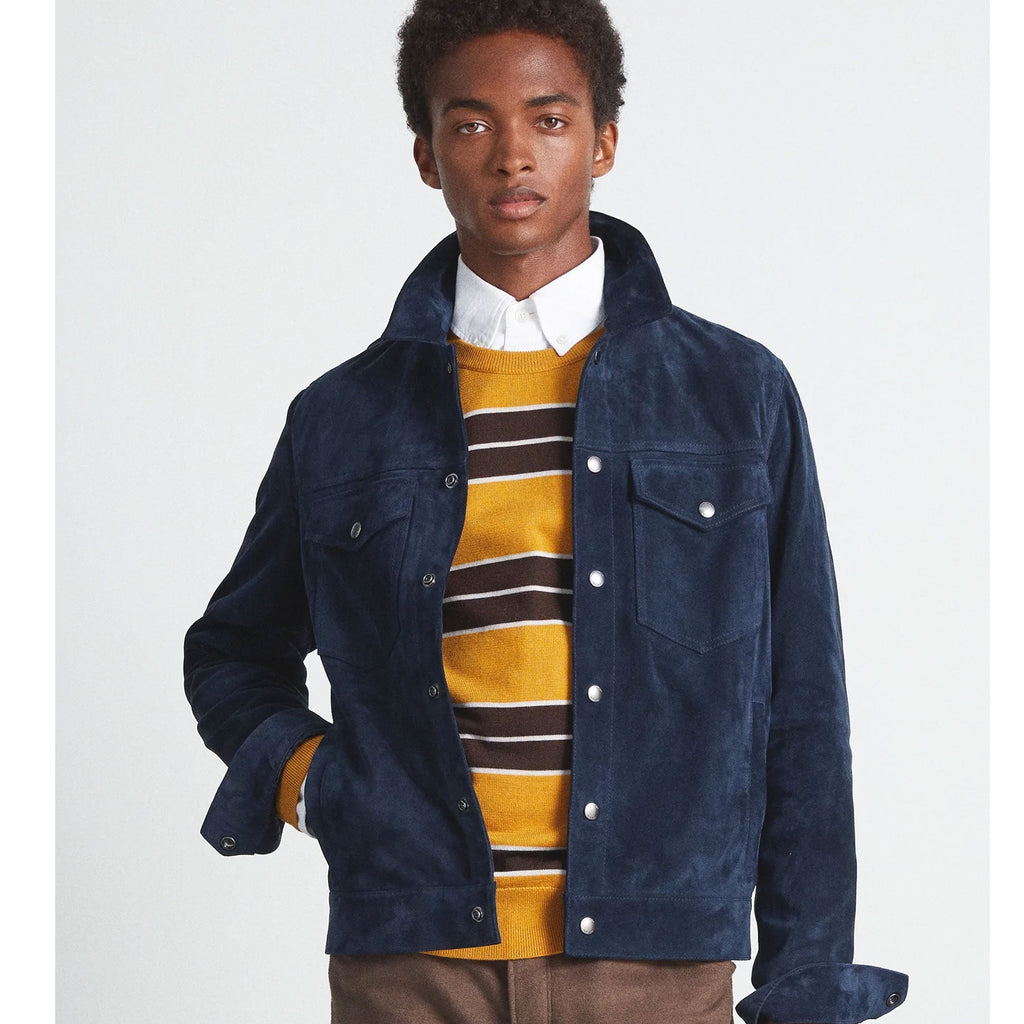 Man wearing a navy jacket over a mustard yellow striped sweater on a white background