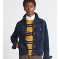 Man wearing a navy jacket over a mustard yellow striped sweater on a white background