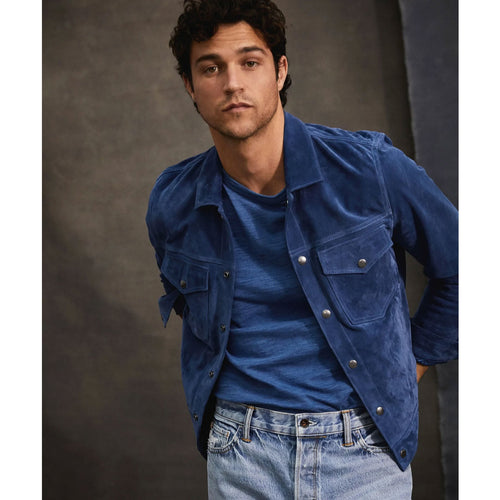 Man wearing a blue jacket over a blue shirt with jeans against a dark background