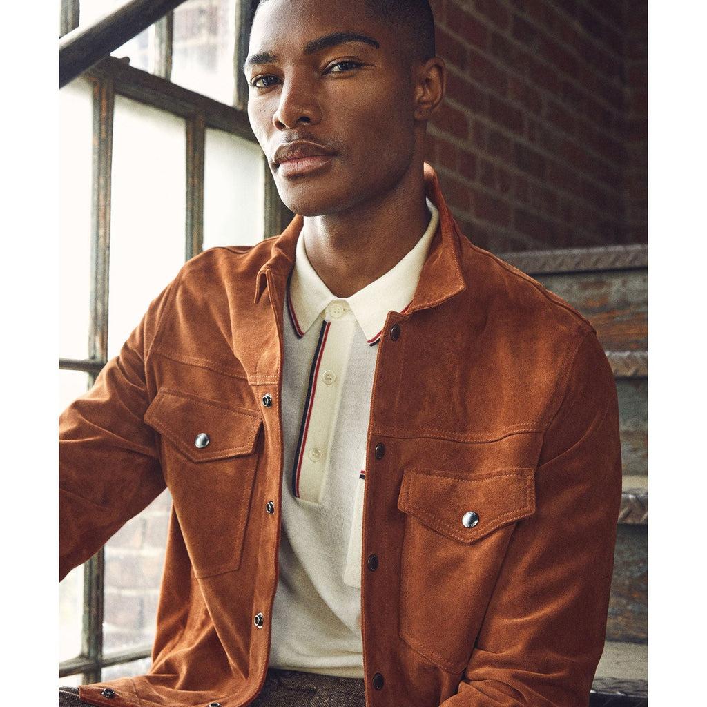 Man wearing a brown suede jacket indoors with a brick wall background
