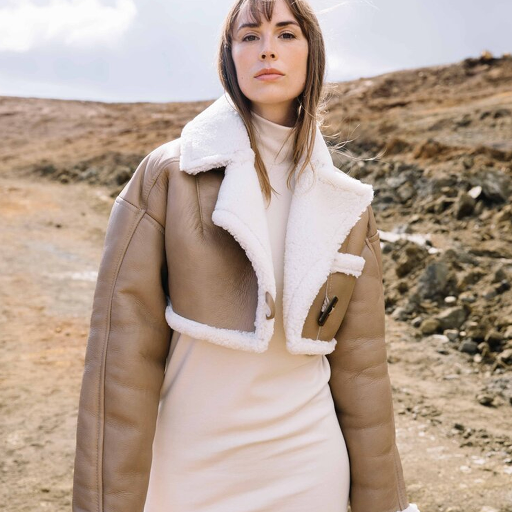 Woman wearing a beige coat with white fur lining in a desert-like setting