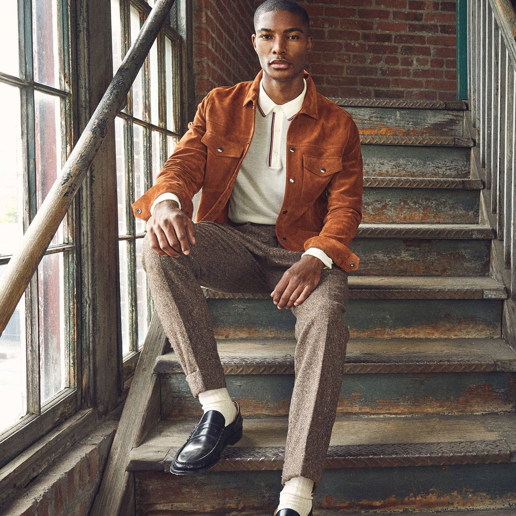 Man in an orange jacket and brown pants sitting on a staircase.