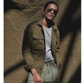 Man wearing a green jacket and sunglasses against a textured brown background