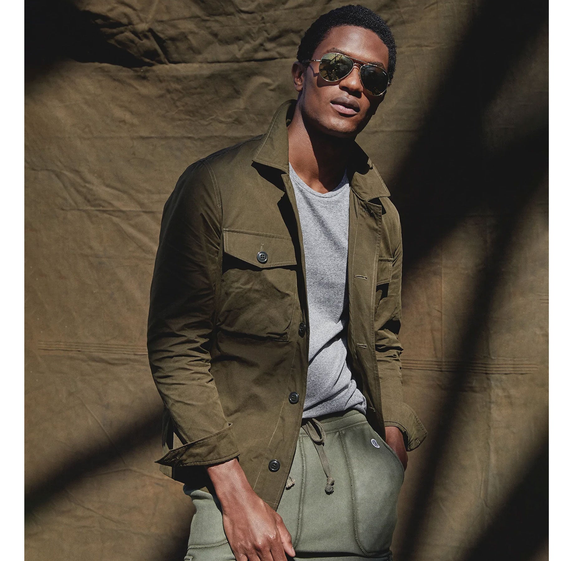 Man wearing a green jacket and sunglasses against a textured brown background