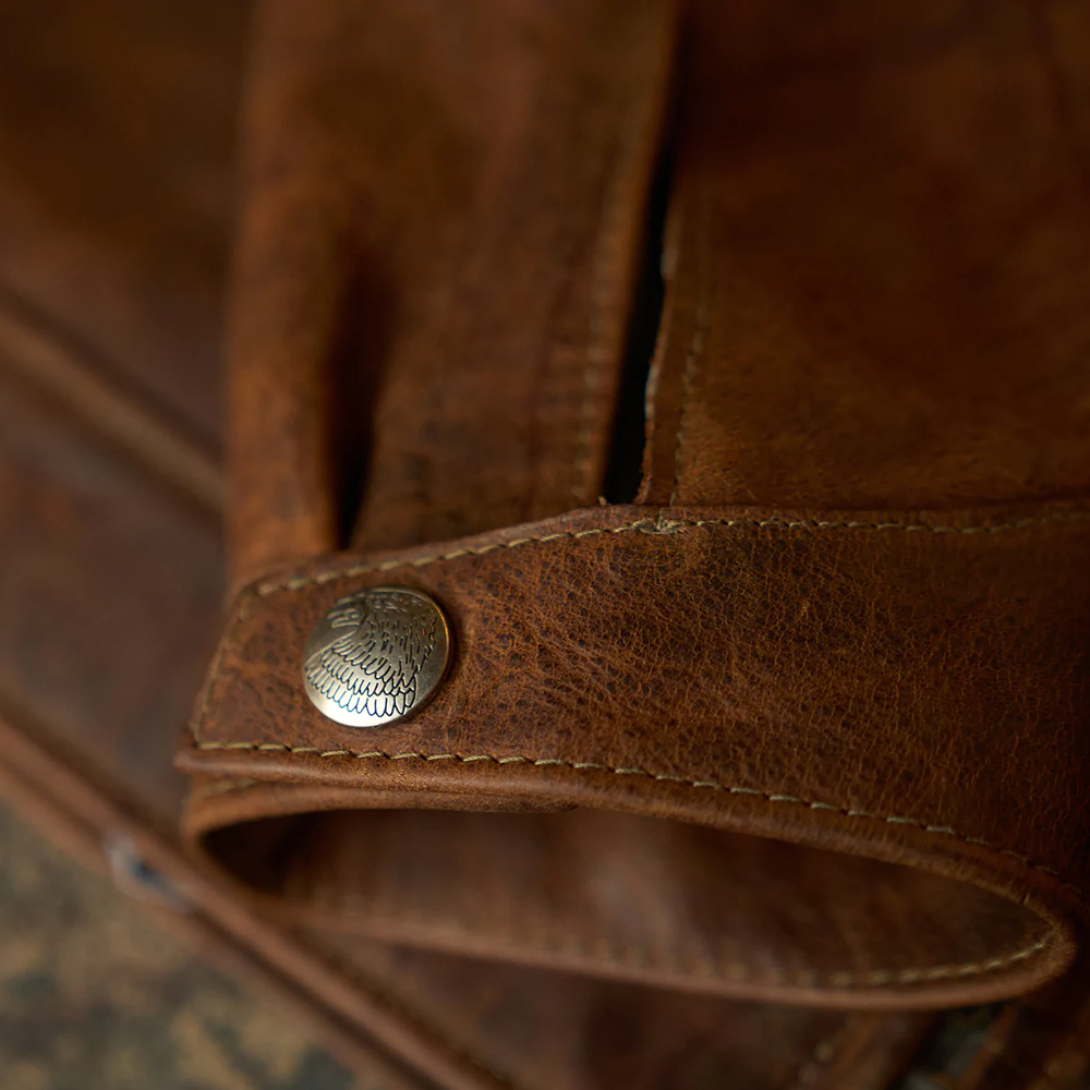 Close-up of a brown leather jacket with a metal button.