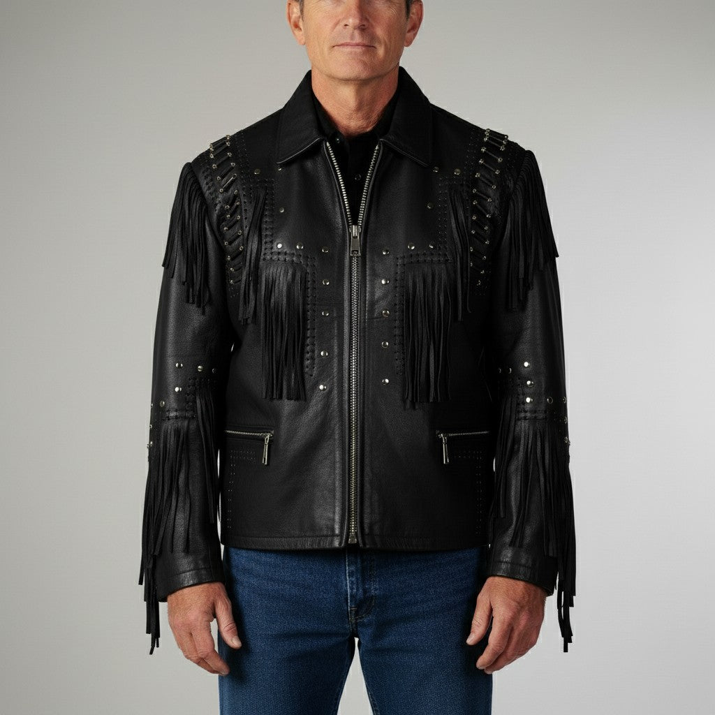 A man wearing a black leather motorcycle jacket with fringe, studded details, and silver zippers, paired with blue jeans, against a neutral gray background.