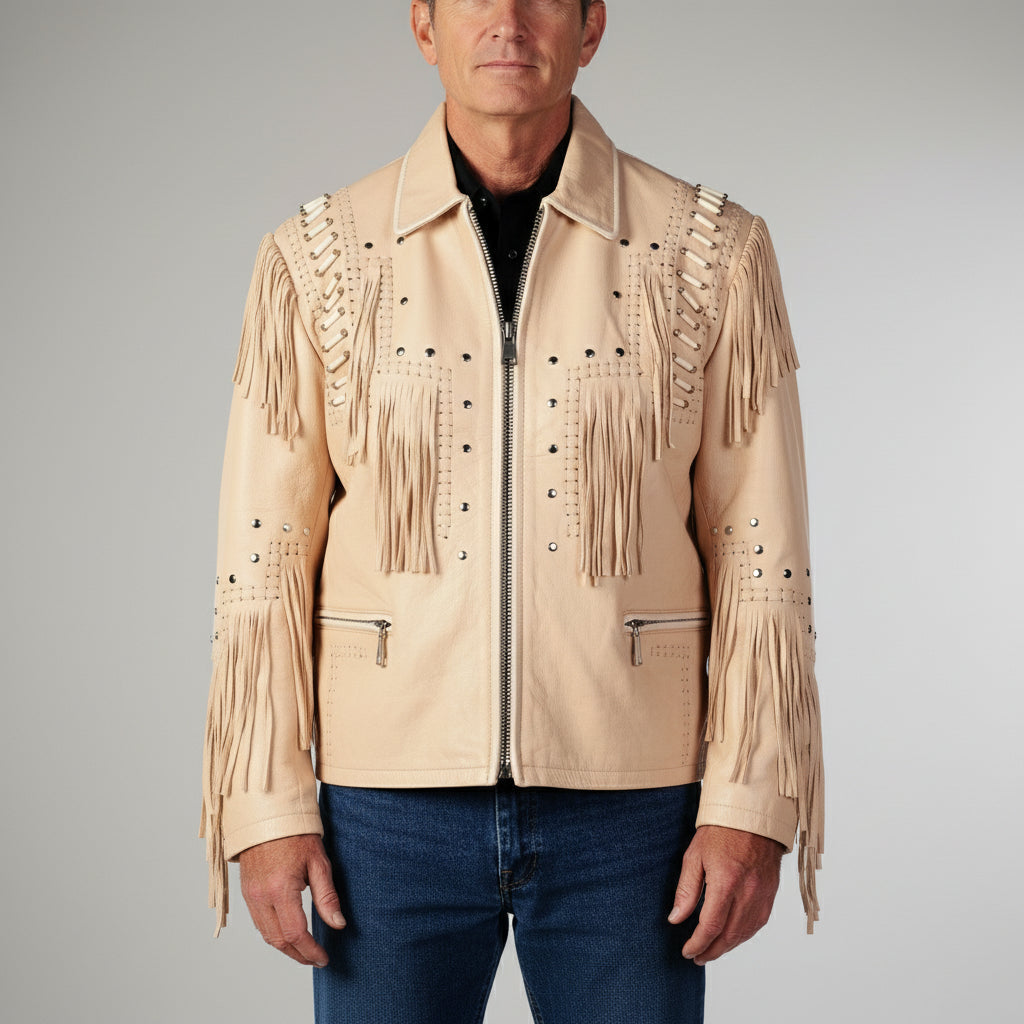 A man wearing a beige fringed leather jacket with silver studs and zippers, paired with blue jeans, photographed against a neutral gray studio background.