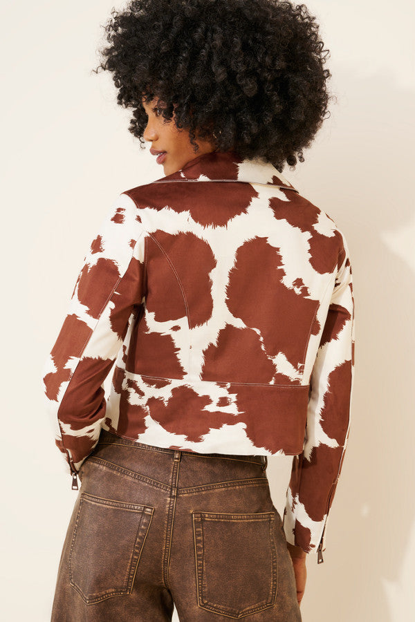 Person wearing a brown and white cow print jacket on a plain background
