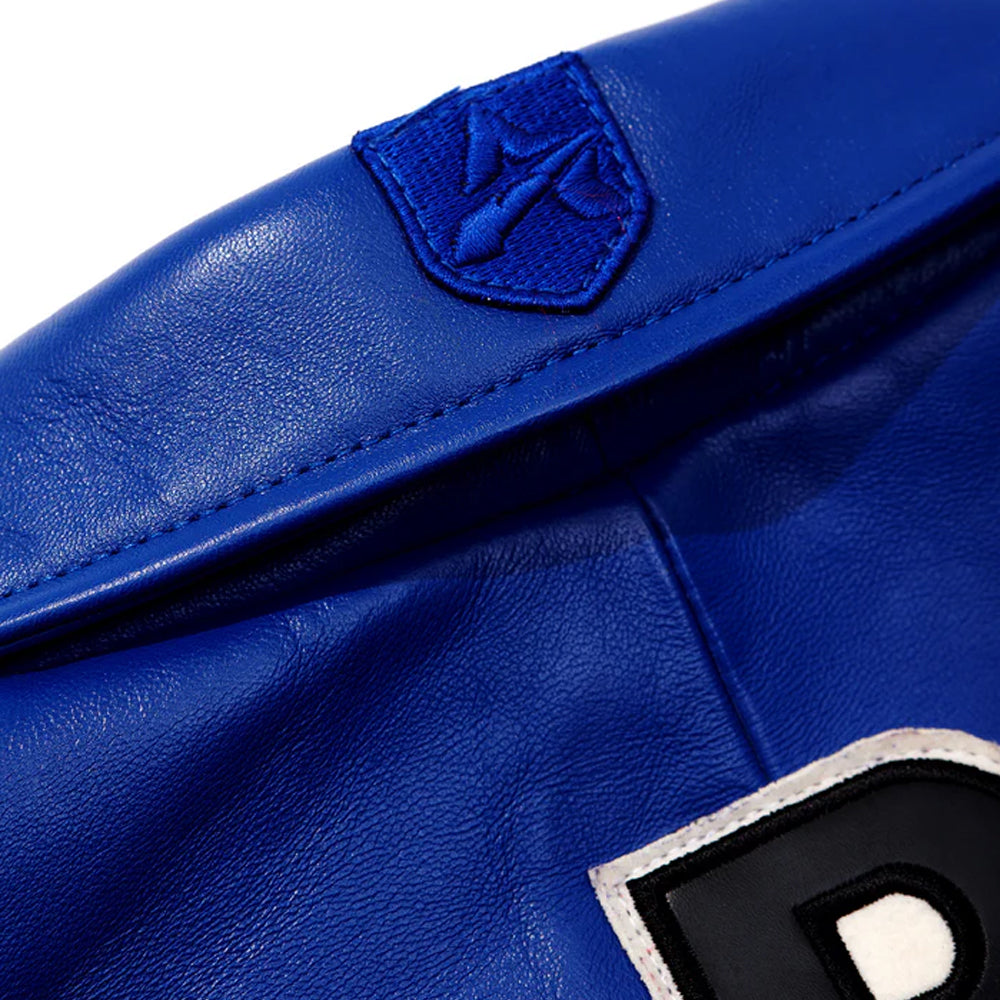 Close-up of a royal blue leather jacket showing a matching blue embroidered shield patch on the shoulder and part of a black, white, and blue letter patch.