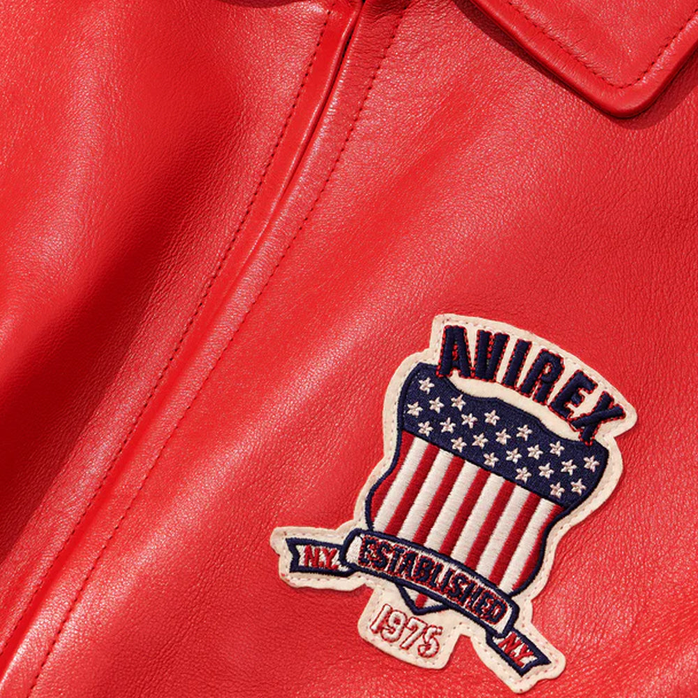 Close-up of a red leather jacket featuring a decorative embroidered patch with the brand name 'AVIREX' and 'NY ESTABLISHED 1975' on a red leather background.