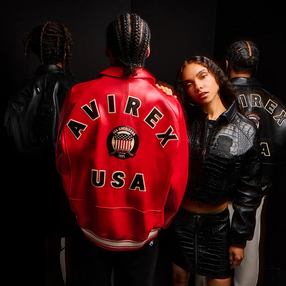 A group of models wearing Avirex leather jackets in a dark studio setting. The central figure is shown from the back wearing a bright red leather varsity-style jacket with 'AVIREX USA' and a circular American flag patch on the back.