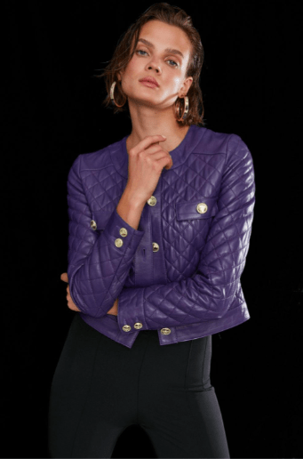 A model wearing a purple quilted leather jacket with gold-tone buttons, paired with black pants, set against a solid black background.