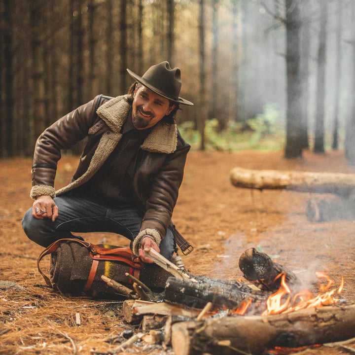 Man in a forest setting with a fire and camping gear