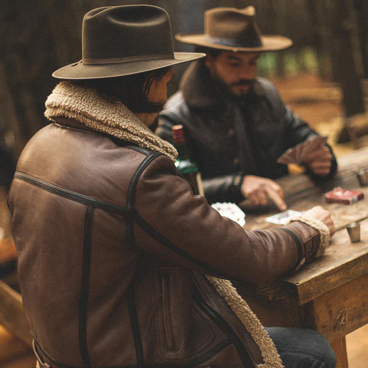 Two men in cowboy hats and leather jackets sitting at a table in a dimly lit room.