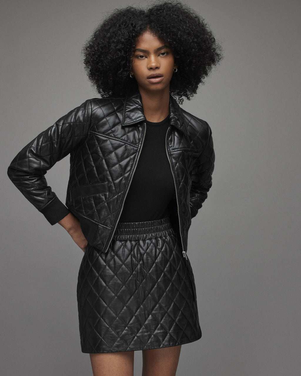 Woman wearing a black quilted jacket and skirt against a gray background