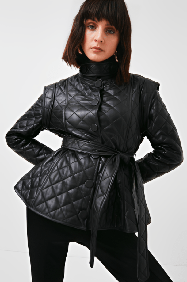 A model wearing a black quilted leather wrap jacket with a high mock neck, button front, and self-tie belt, paired with black pants against a light gray studio background.