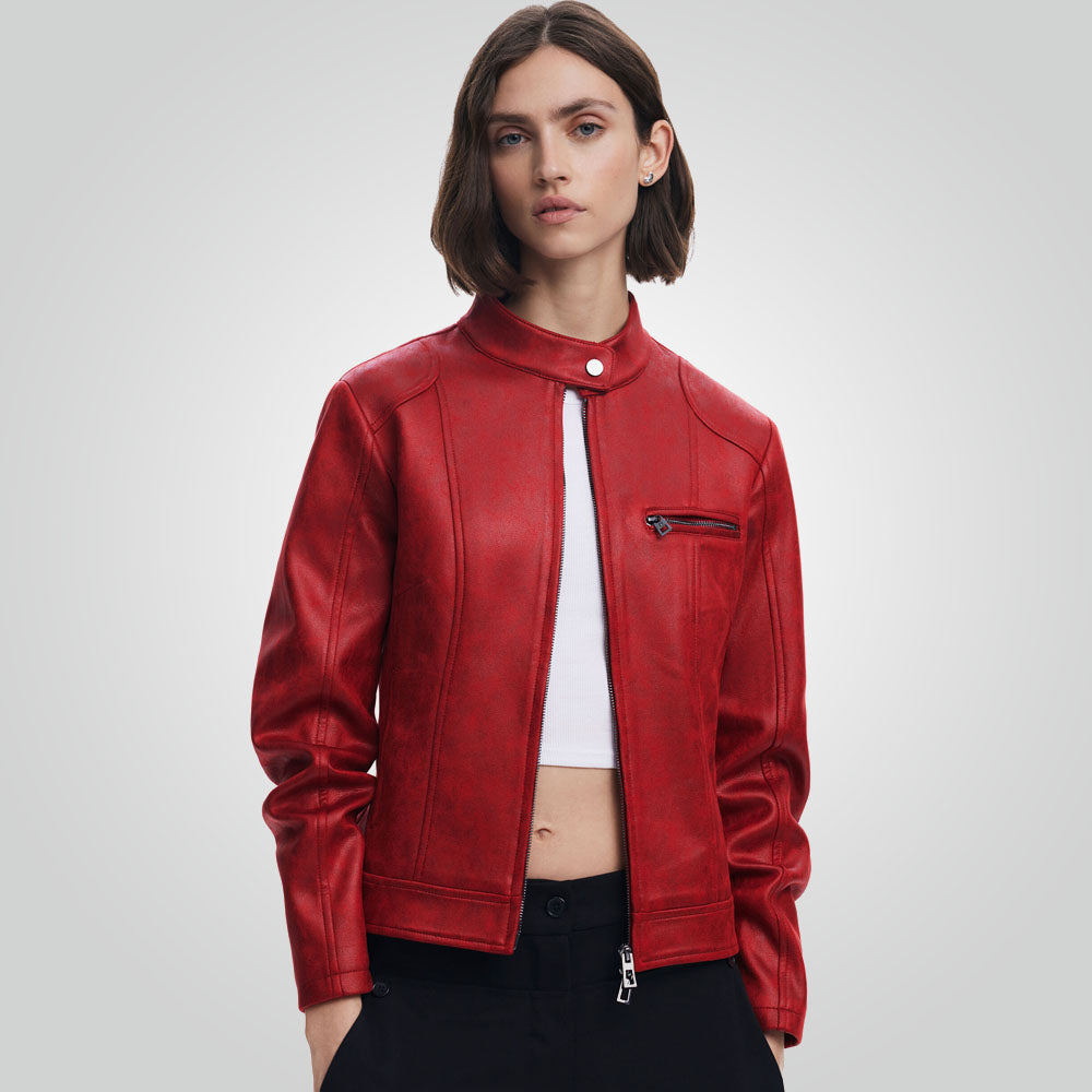 A woman modeling a cropped red faux-leather moto jacket with a stand-up collar, zippered front, and zippered chest pocket, worn over a white crop top and black pants against a light gray studio background.