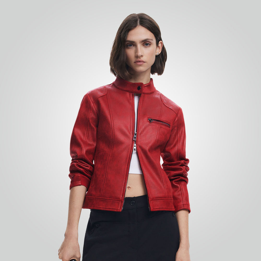 A woman modeling a cropped red faux-leather moto jacket with a high collar, front zipper, and zippered chest pocket, paired with black pants against a light gray studio background.