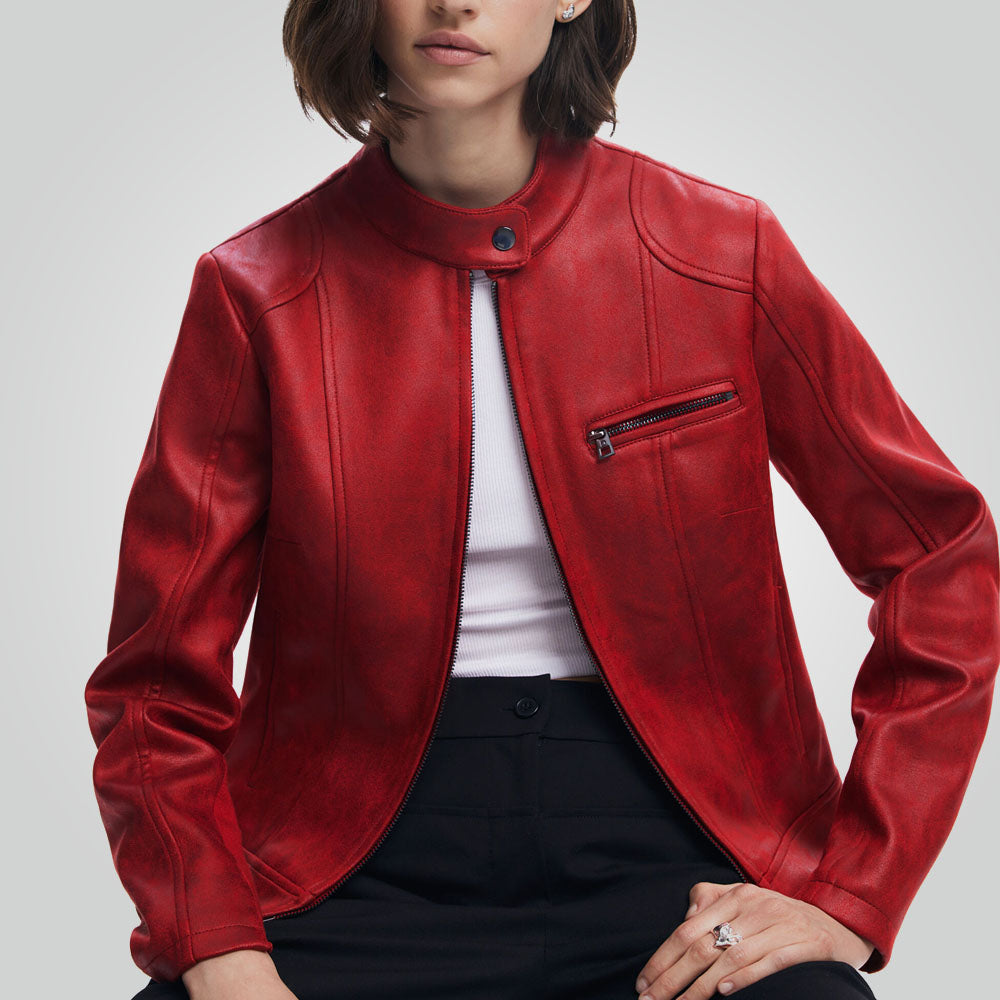 A woman wearing a red faux leather moto jacket with a mock neck, zippered chest pocket, and ribbed cuffs, styled over a white top and black pants against a light gray studio background.