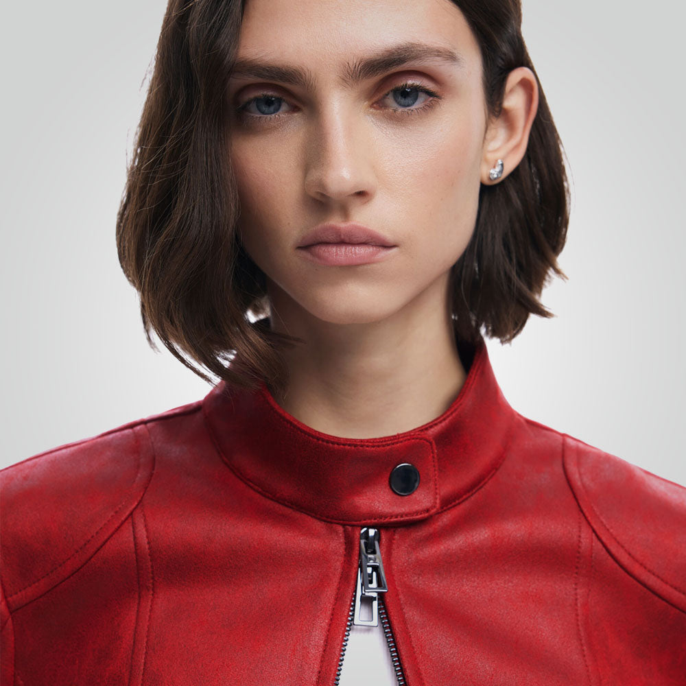 Close-up of a model wearing a vibrant red leather jacket with a high collar and a silver zipper, set against a plain light gray background.