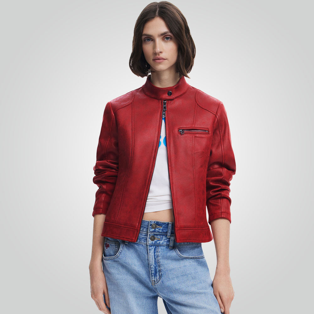 A model wearing a red faux-leather moto jacket with a mock neck, front zipper, and zippered chest pocket, styled with a white crop top and light blue jeans against a light gray studio background.