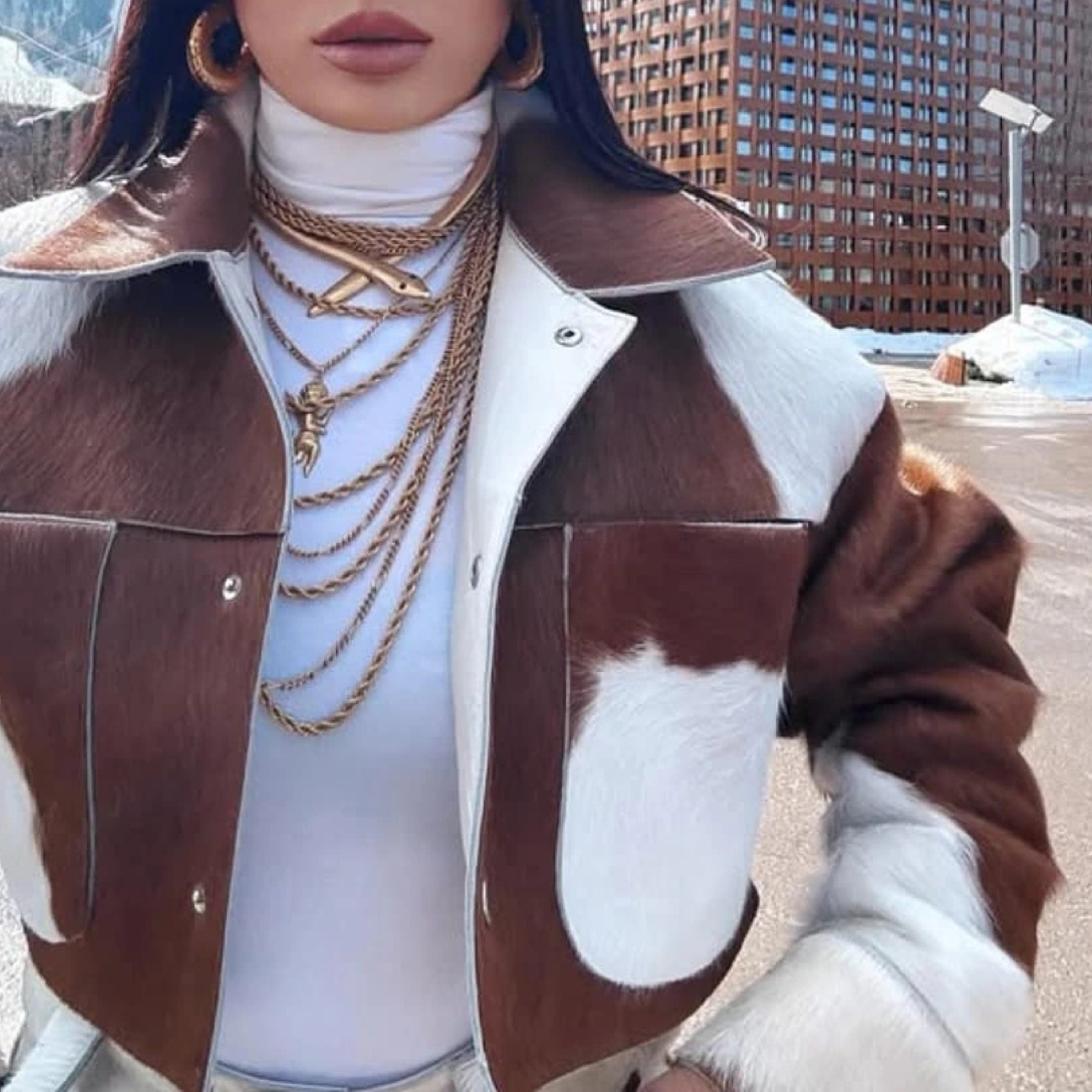 women wearing a brown and white jacket with gold jewelry in an urban setting