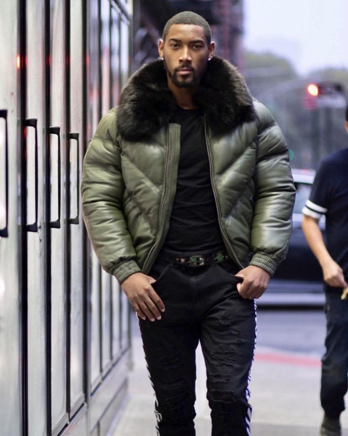 Man wearing a green puffer jacket with fox fur collar in an urban setting