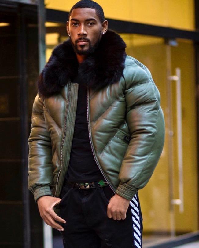 Man wearing a green goose country jacket with a fur-lined hood in an urban setting.