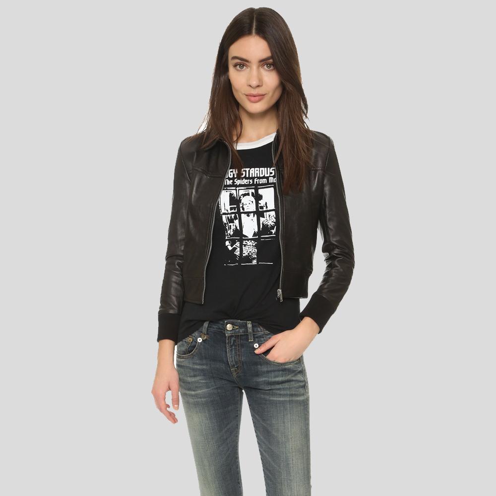 Woman wearing a black leather jacket, black graphic t-shirt, and blue jeans on a gray background