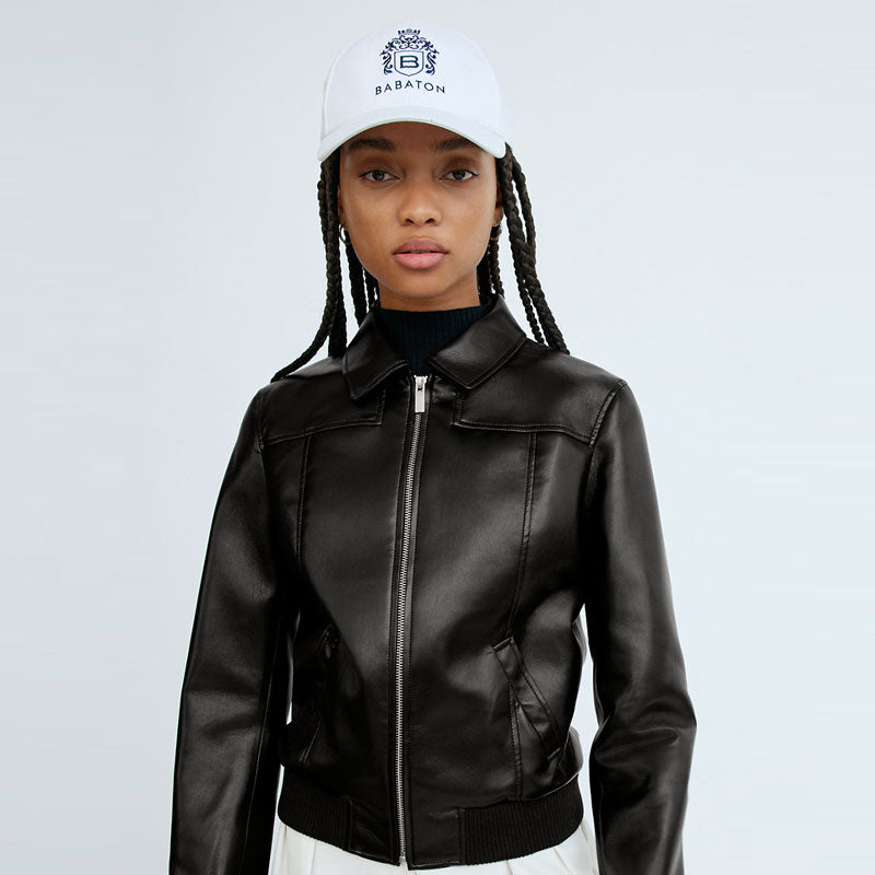 Person wearing a black leather jacket and white cap with a brand logo on a light gray background