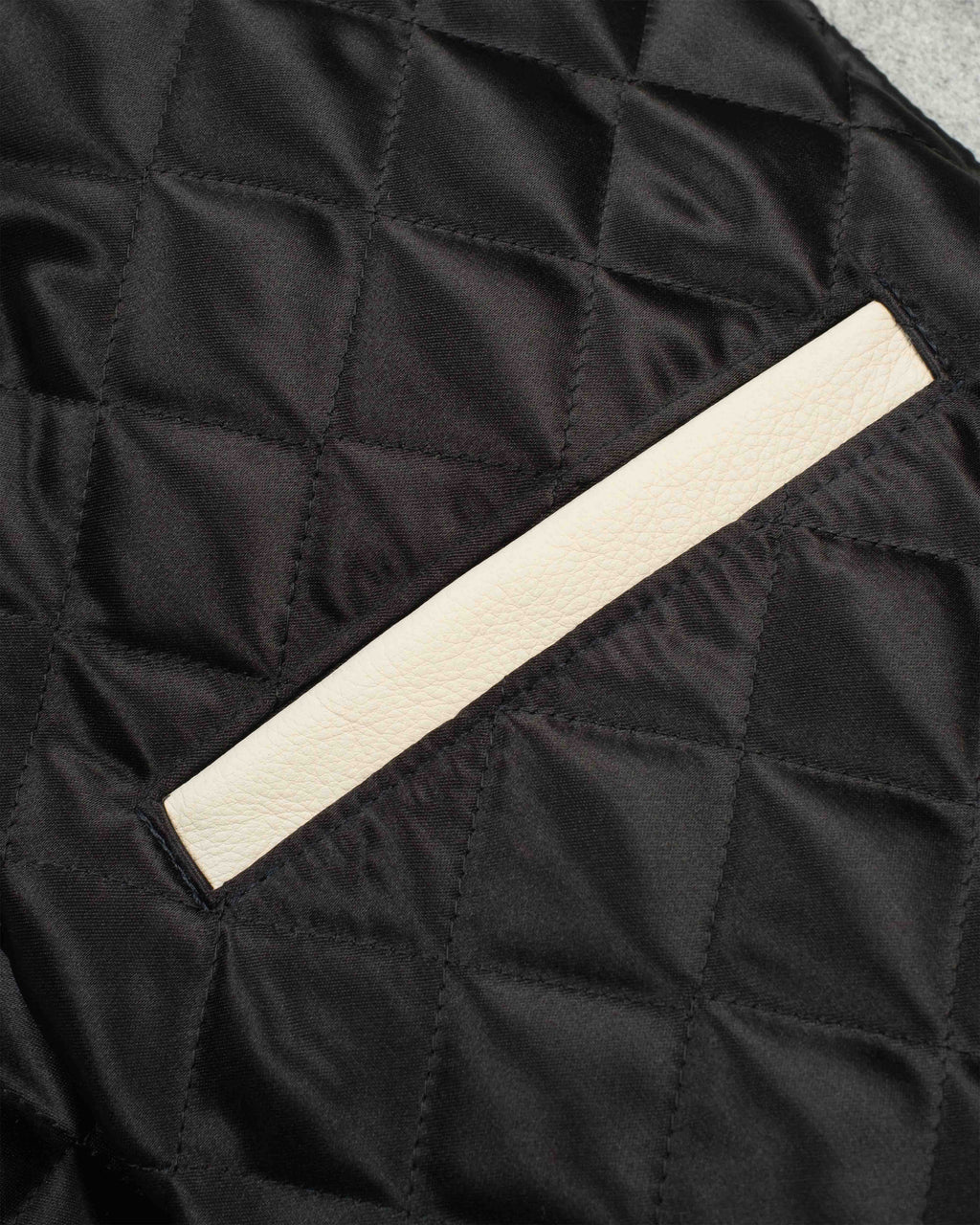 Close-up of a black quilted fabric surface with a diagonal off-white leather trim detail.