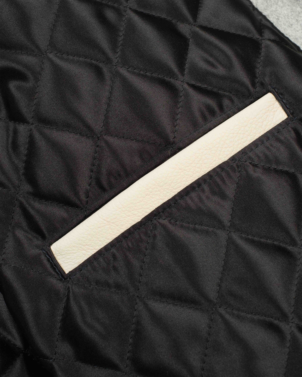 Close-up of a black quilted fabric surface with a diagonal off-white leather trim detail.