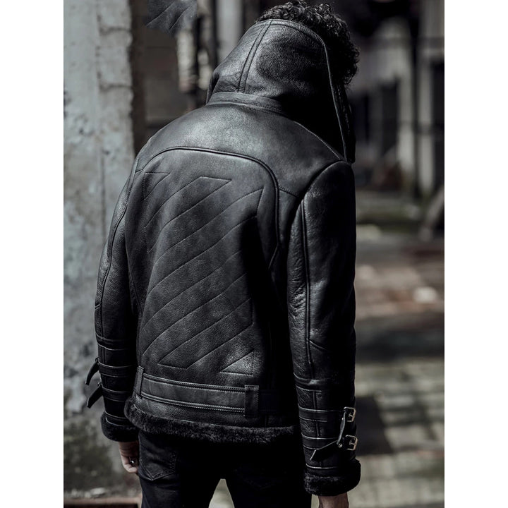 A man viewed from behind wearing a black leather hooded jacket with quilted back paneling and faux-fur trim, standing in an outdoor urban setting.