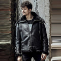 Man wearing a black leather jacket standing against a textured wall.