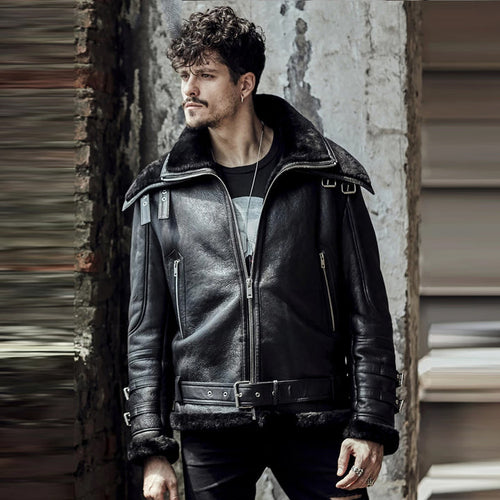 Man wearing a black leather jacket standing against a textured wall.