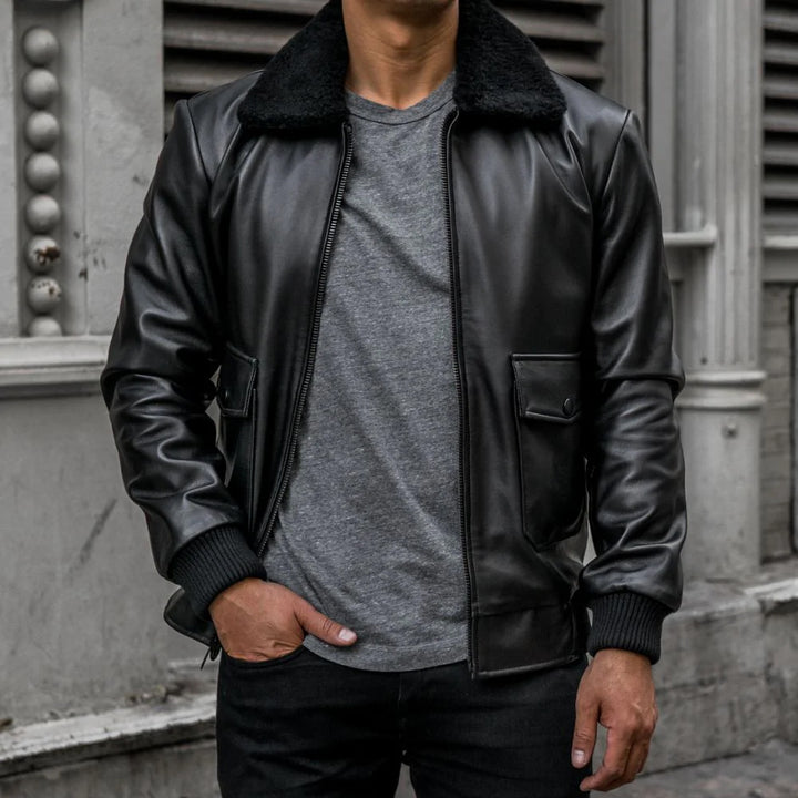 Person wearing a black leather jacket with a gray shirt underneath, standing against a building.