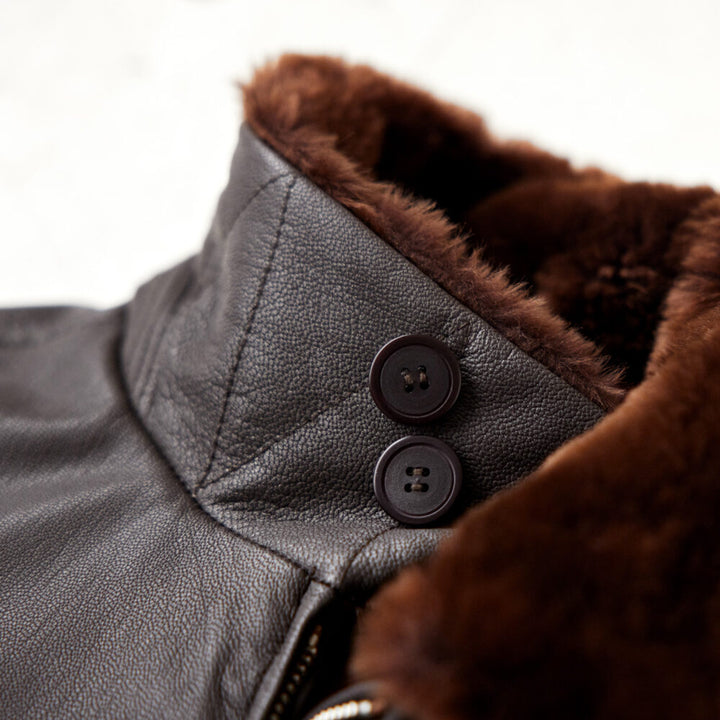 Close-up of a leather jacket with brown fur lining and two buttons.