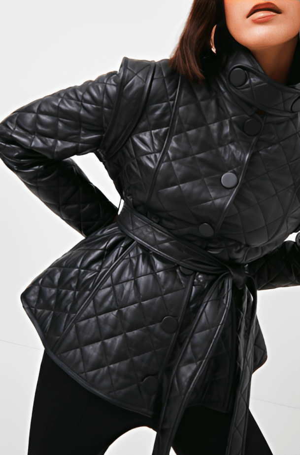 A close-up of a model wearing a black quilted leather belted jacket with a high collar and large buttons, set against a plain light background.