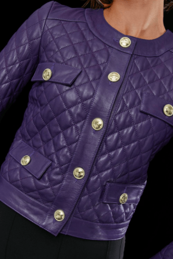 A close-up of a purple quilted leather jacket with prominent gold-tone buttons and flap pockets, shown on a model against a black background.