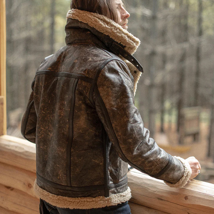 Person wearing a brown leather jacket with fur lining, standing by a wooden railing.
