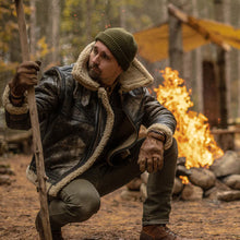 Man in winter clothing crouching near a fire in a forest
