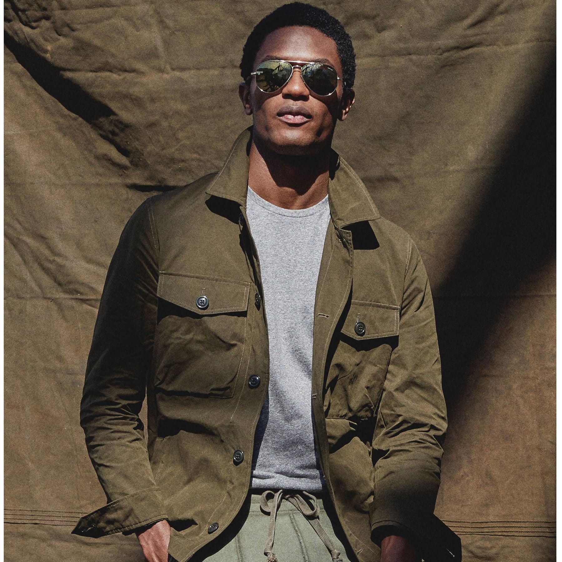 Man wearing a green jacket and sunglasses against a brown textured background