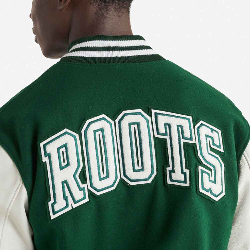 Close-up back view of a person wearing a green varsity-style jacket with large white and green 'ROOTS' lettering across the back and white sleeves.