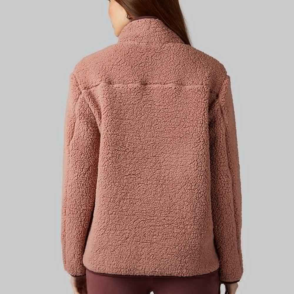 A woman viewed from the back wearing a dusty rose sherpa fleece jacket against a solid gray background.