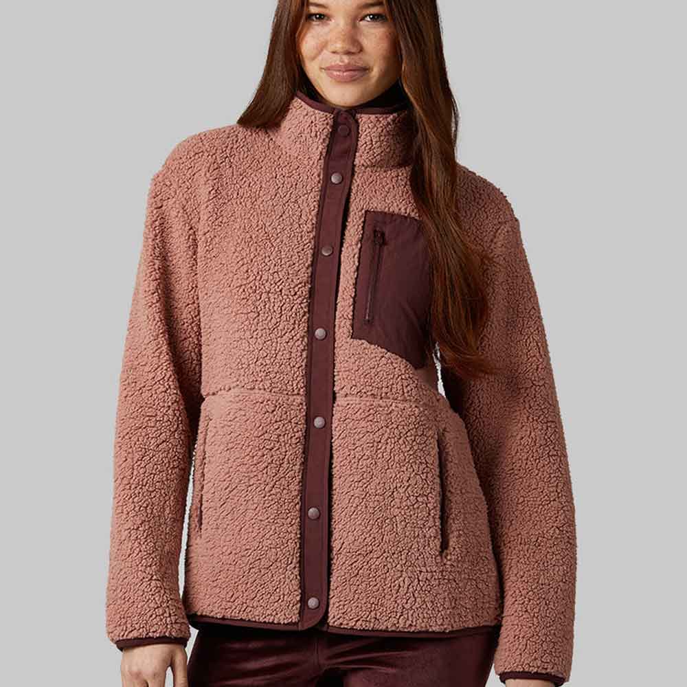 A woman wearing a dusty rose sherpa fleece jacket with dark brown trim and a button-up front, shown against a solid gray studio background.