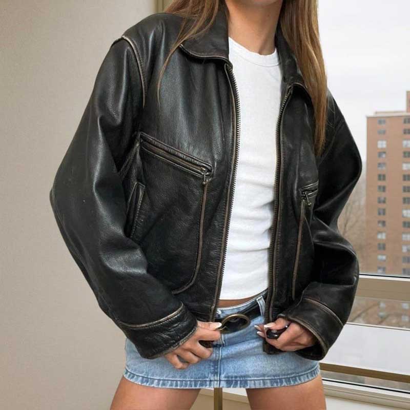 Person wearing a black leather jacket over a white shirt and denim skirt.