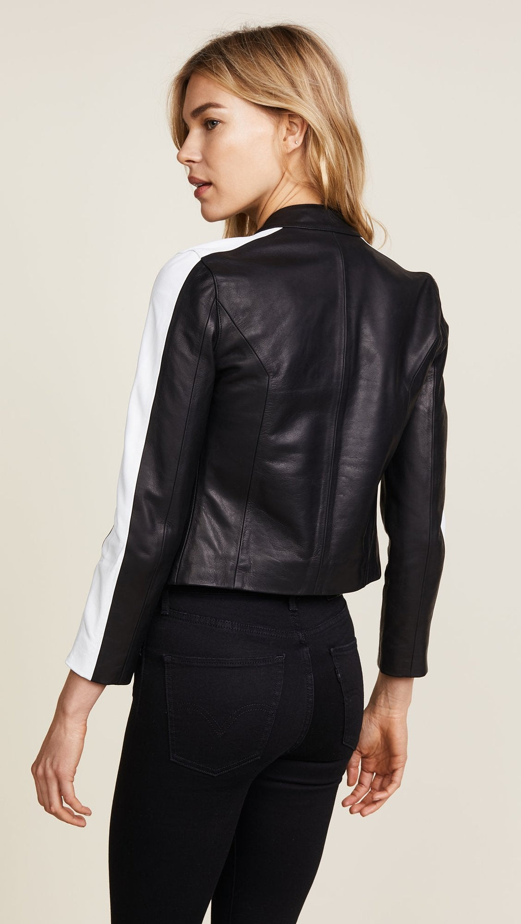 Woman wearing a black leather jacket with a white shirt underneath on a beige background