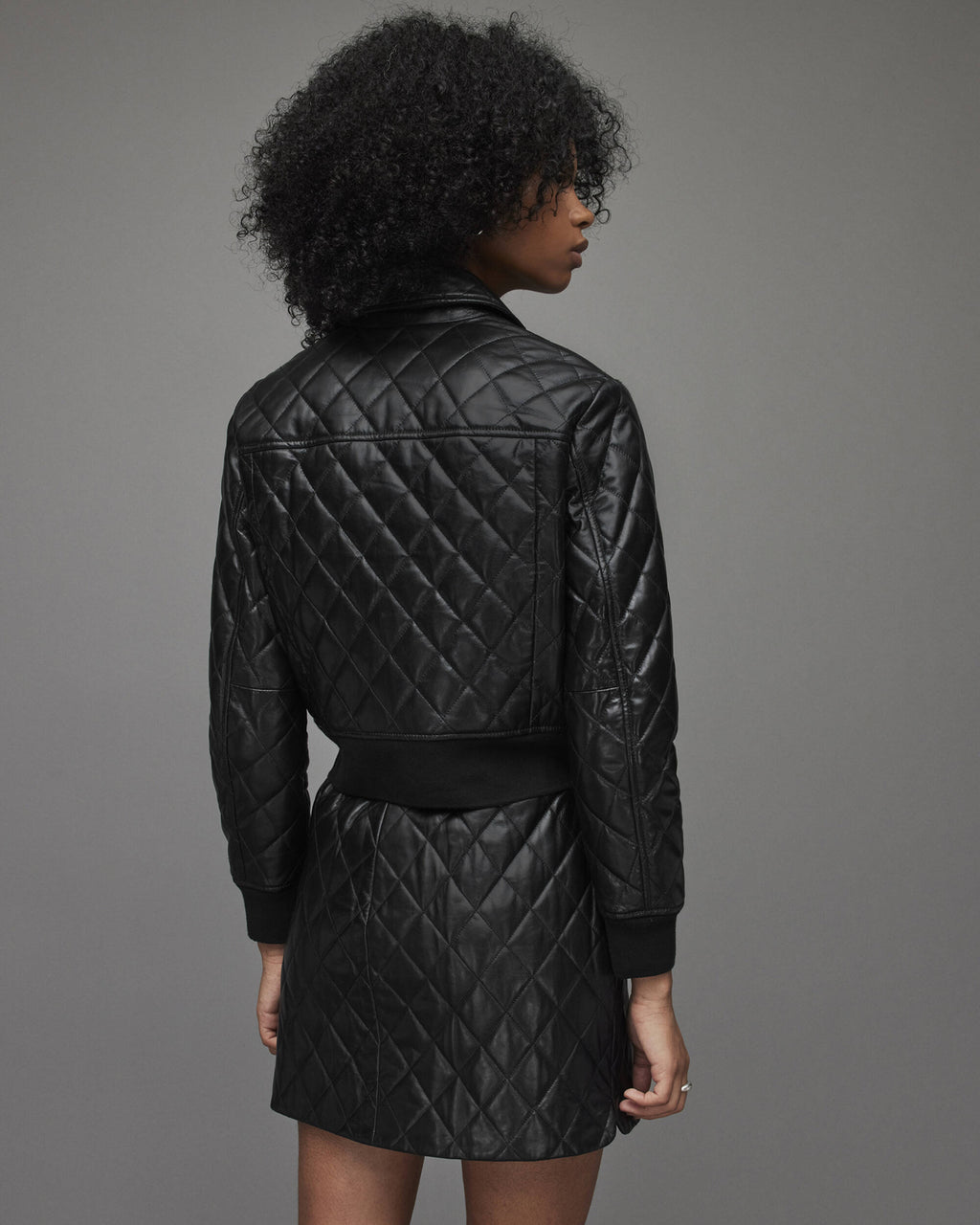 Person wearing a black quilted jacket and skirt set against a gray background
